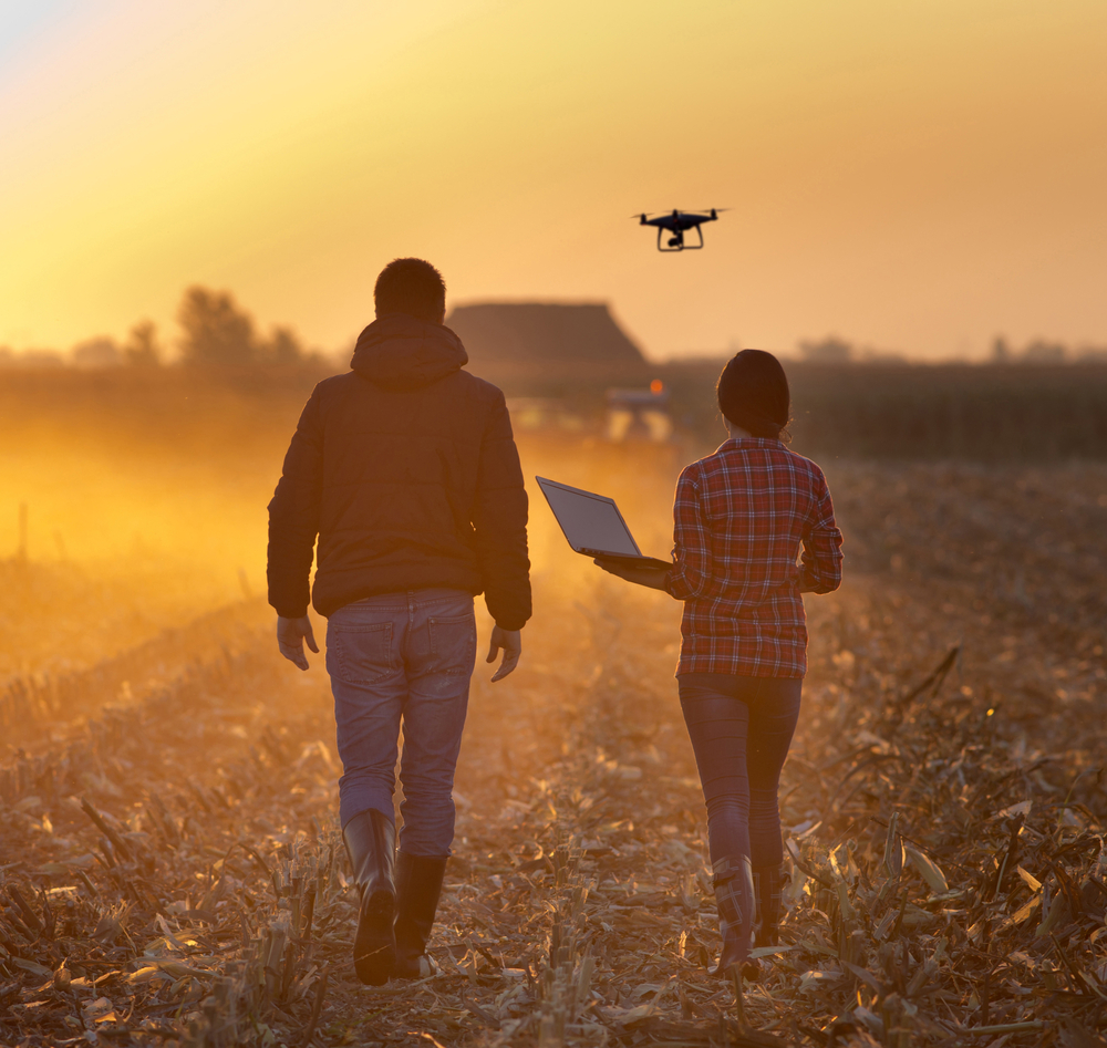 2 people walking through a field flying a drone