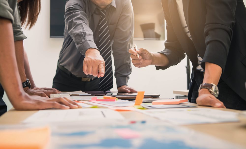 Three people standing around paperwork on a desk planning