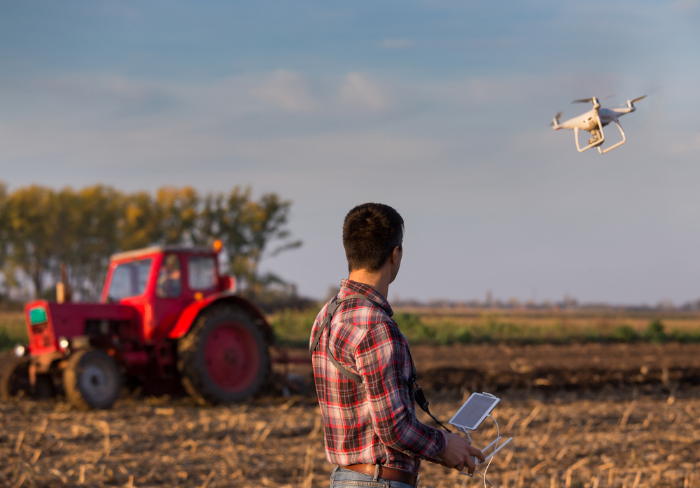 Person flying a drone with a red tractor in the background